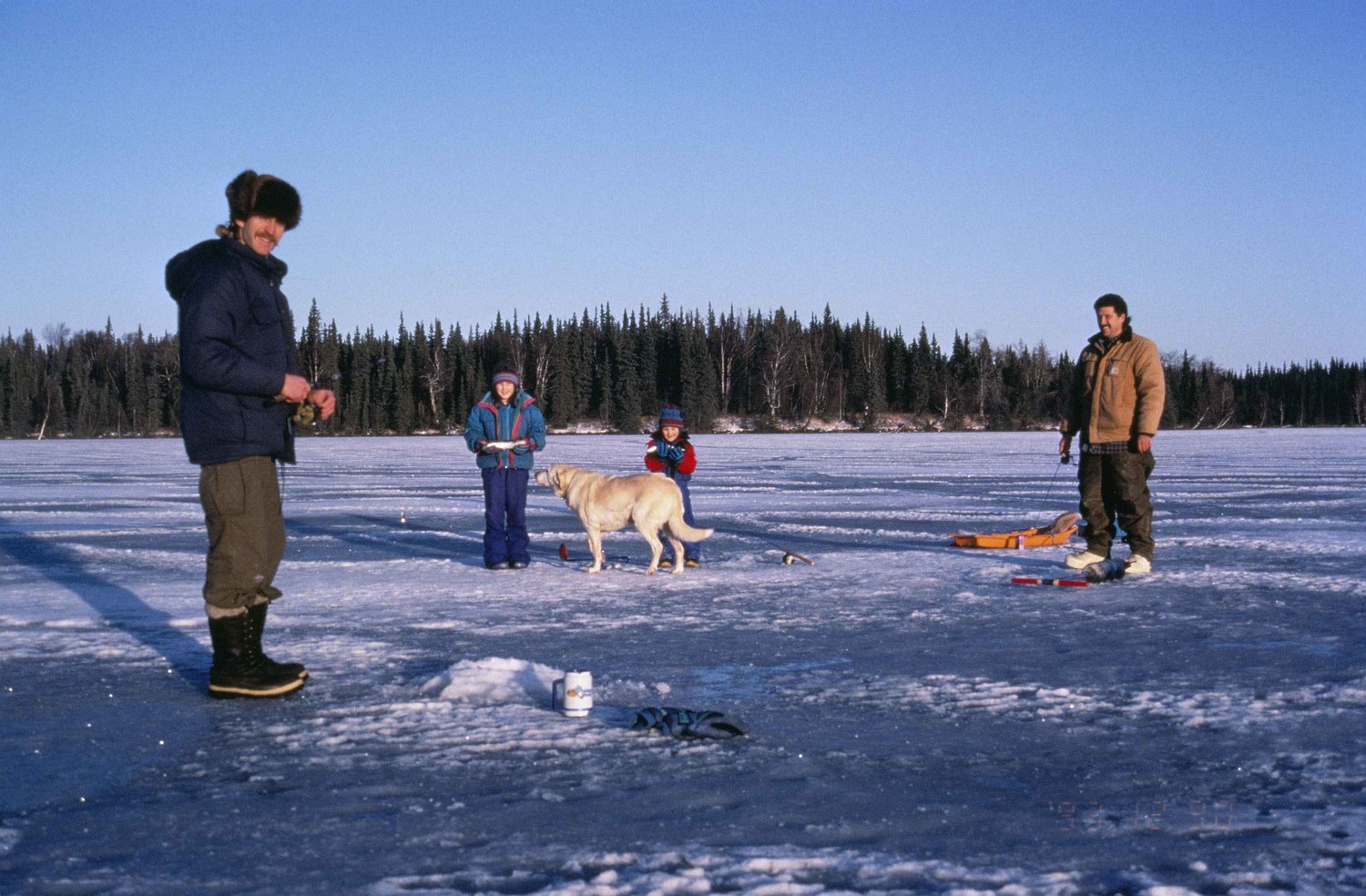 Two men, kids, and a dog enjoy ice fishing.